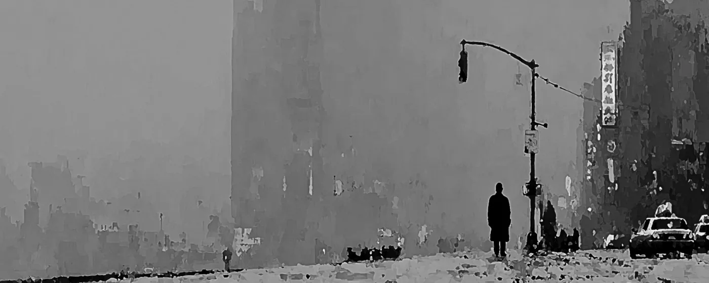 A grayscale city street with a pedestrian standing beside traffic lights